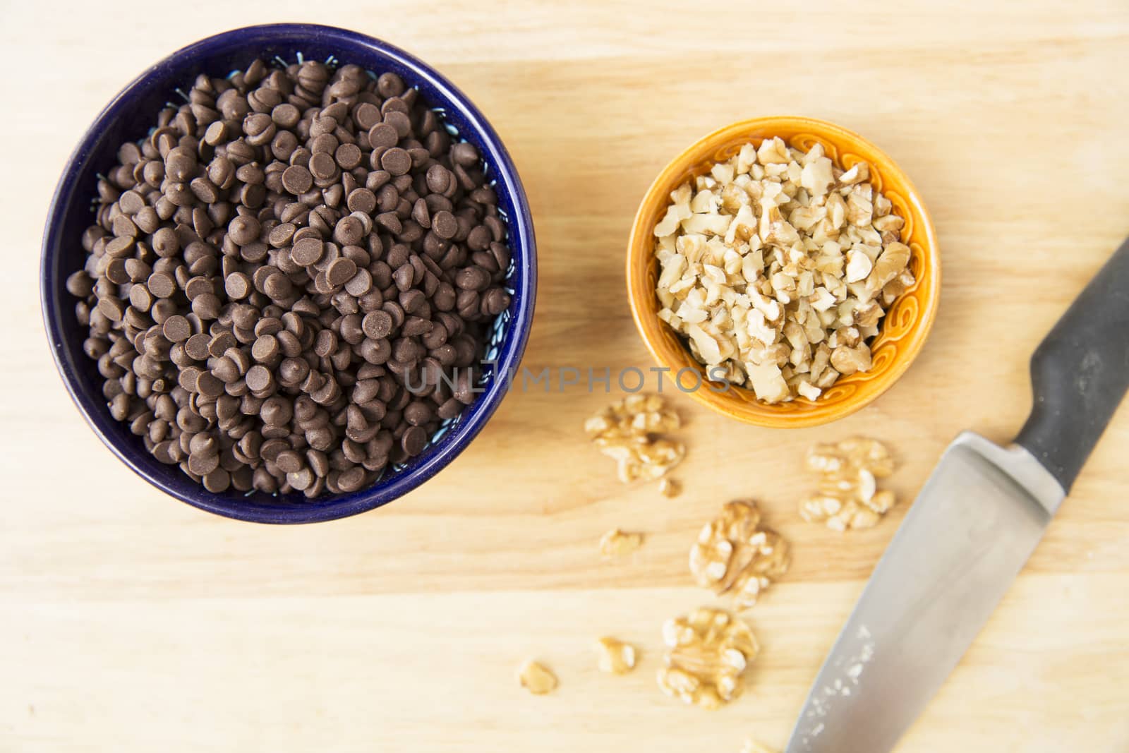 Chocolate chips and chopped walnuts in bowl with knife, viewed from above.
