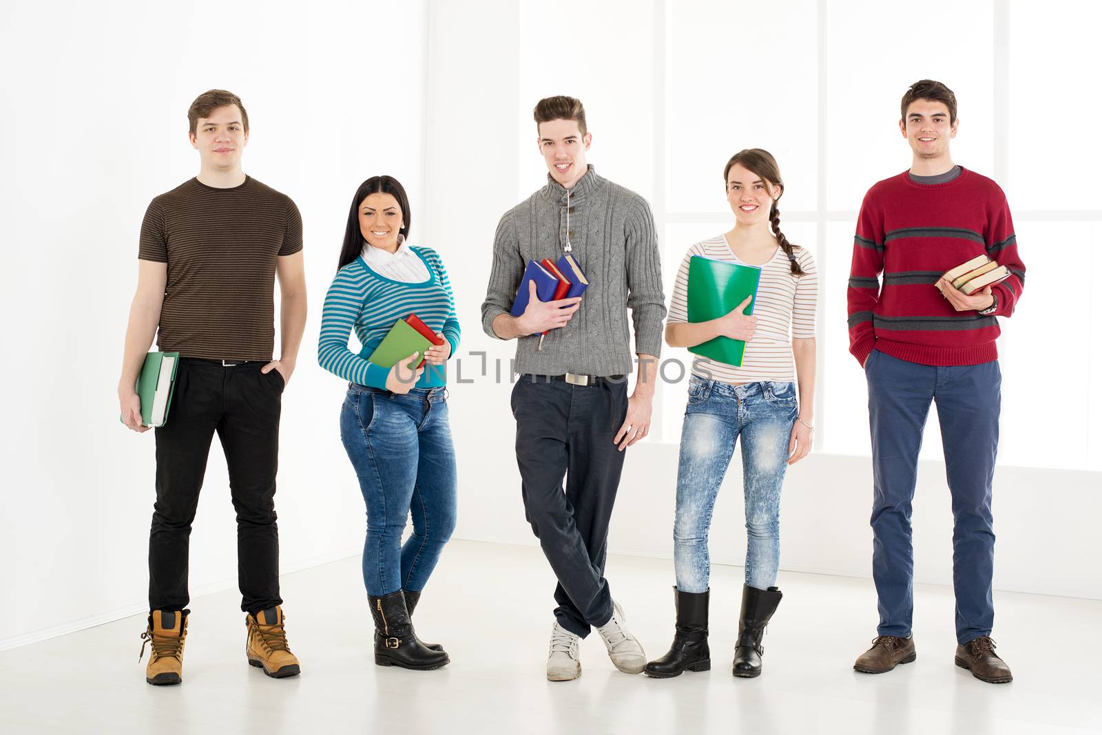 Group of cheerful students with books standing in school hall and looking at camera.