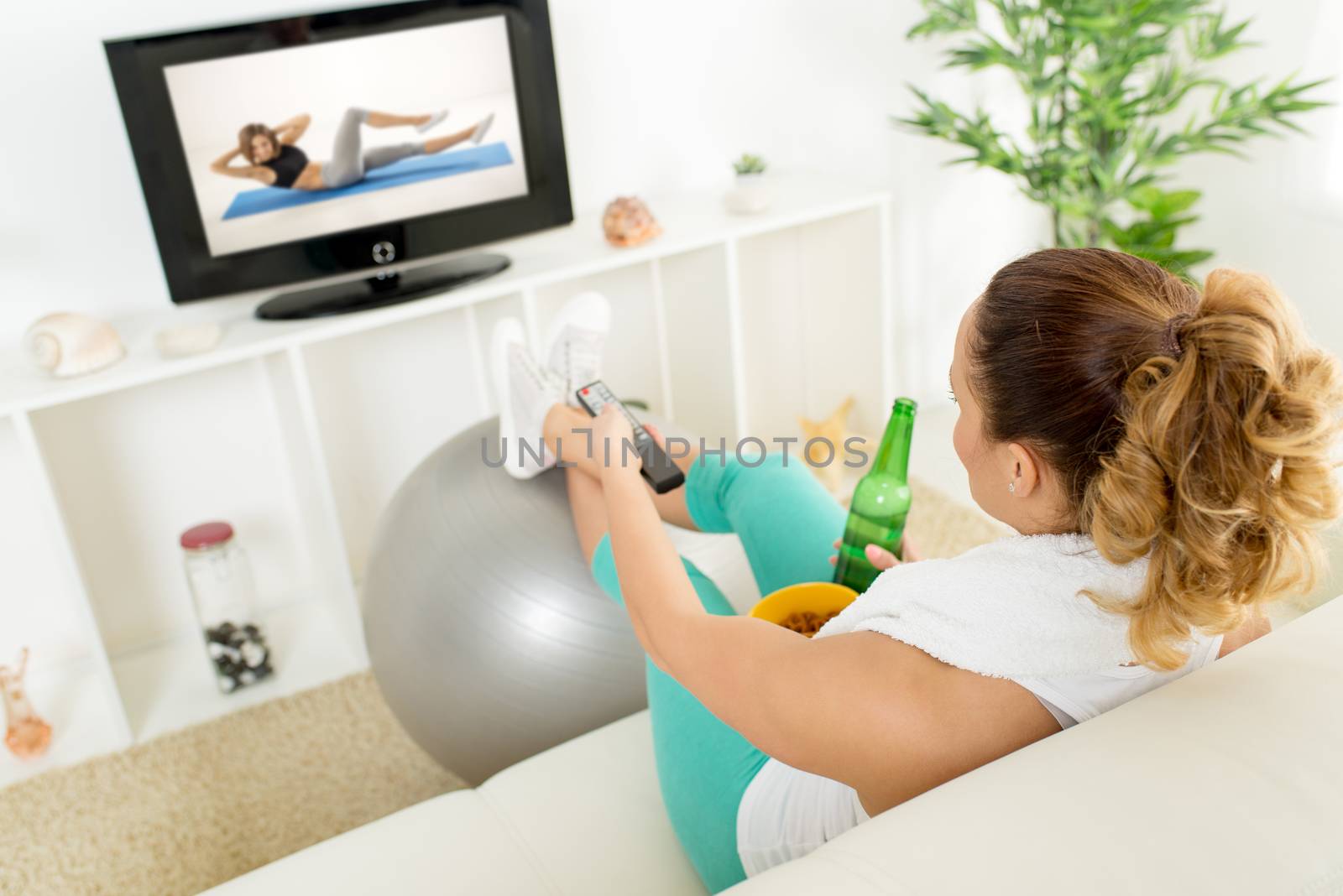 Lazy woman in sport clothing sitting front of the TV and doesn't wont to exercise.