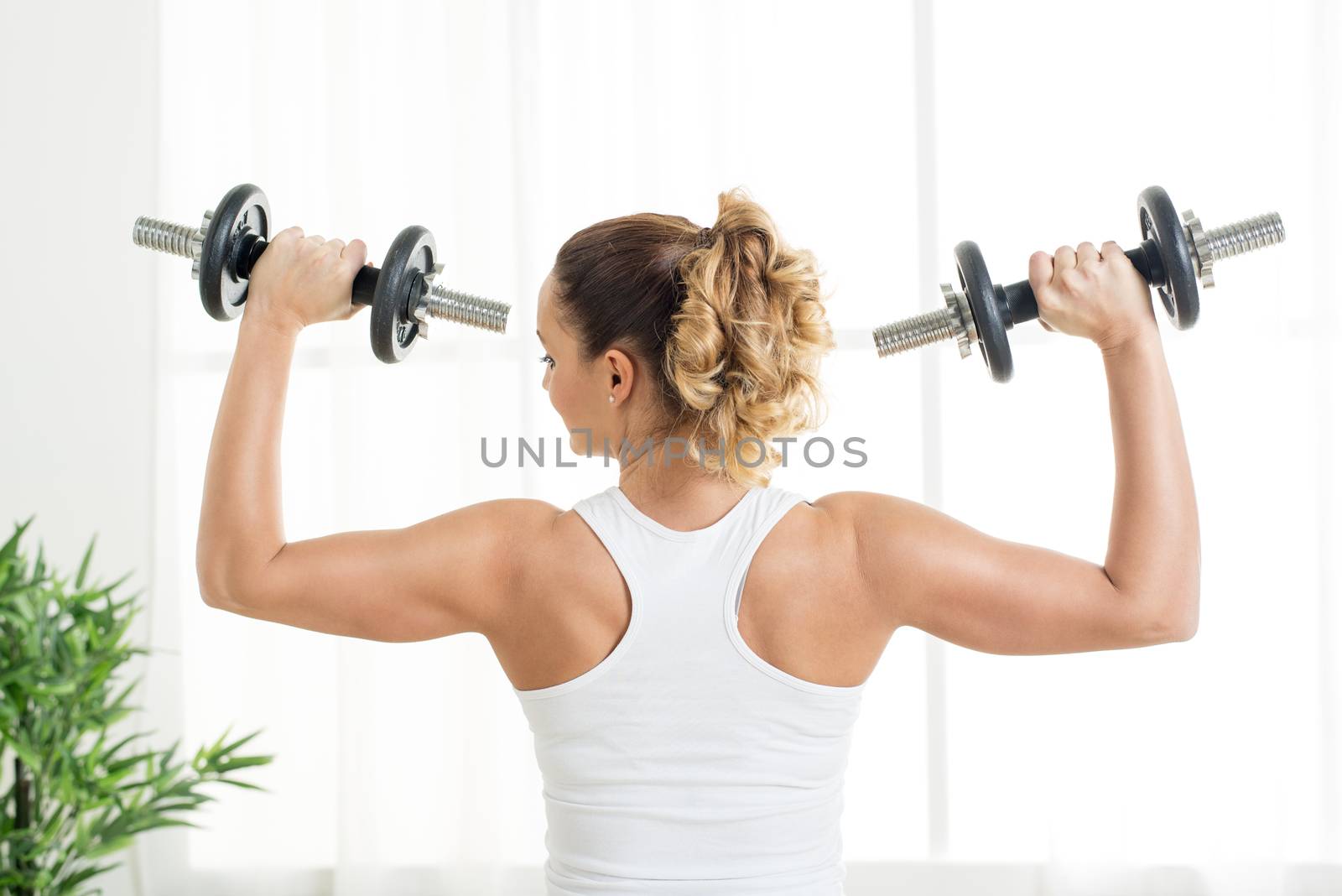 Beautiful young woman doing exercise to strengthen shoulder with dumbbells at home.