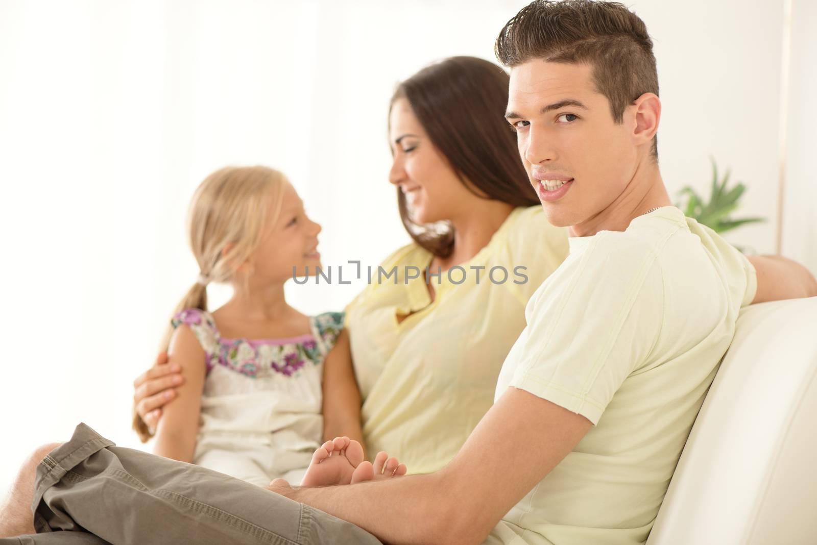 Father is in the foreground and looking at camera. Behind him mom and daughter talking. Selective focus.