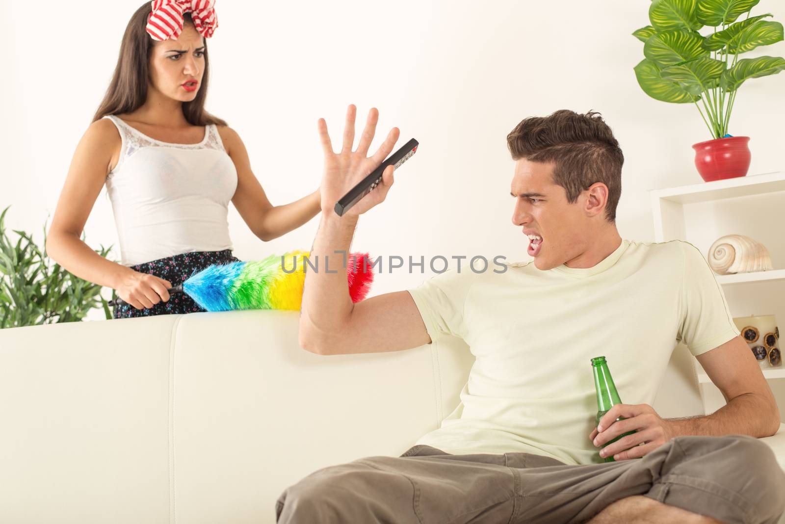 Young man sitting on sofa and watching tv. His angry wife yelling.