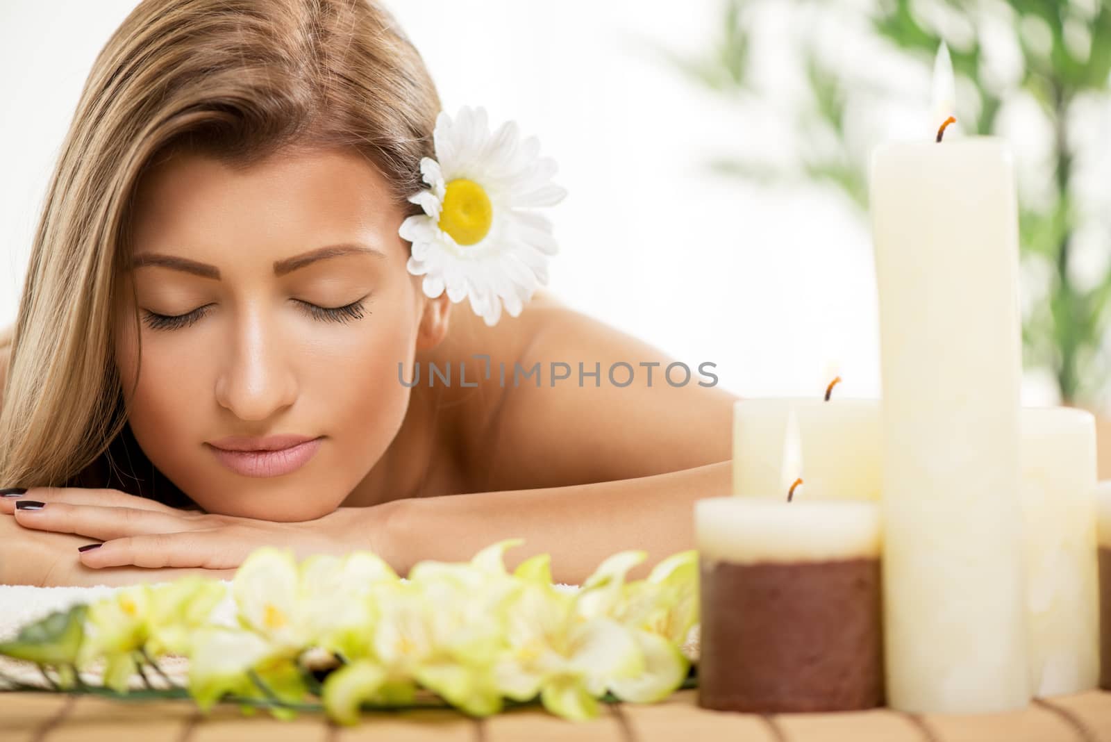 Cute young woman lying on a towel during a skincare treatment at a spa. She is relaxing  and enjoying with eyes closed. 