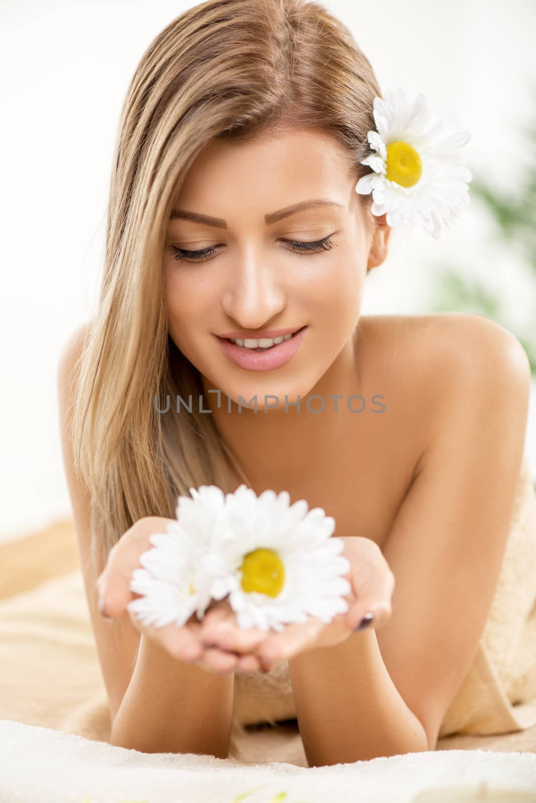 Cute young woman enjoying during a skincare treatment at a spa. She is smiling and holding white flowers in her hands. 