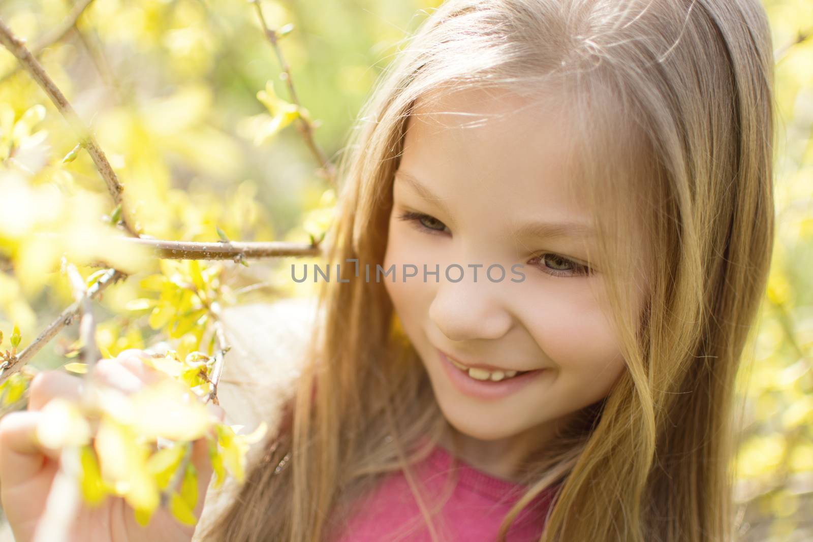 Smiling cute little girl standing beside a flower tree in the park and thinking.