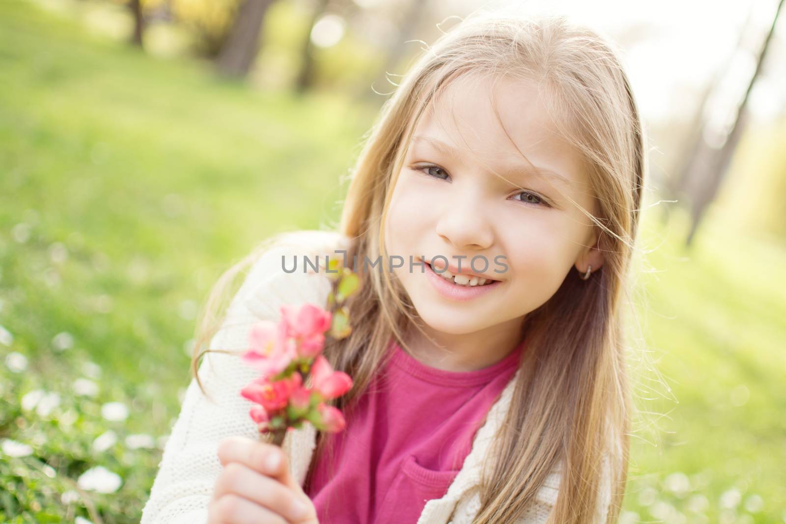 Smiling cute little girl on the meadow in spring holding flower and looking at camera.