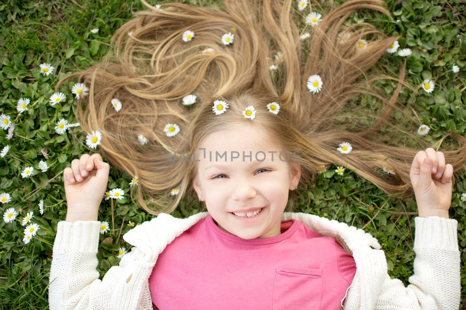 Beautiful smiling little girl lying on the flower meadow in spring and looking at camera.