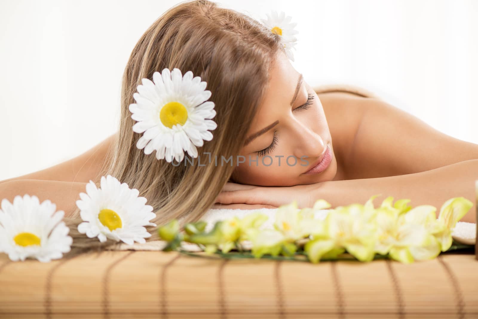 Cute young woman lying on a towel during a skincare treatment at a spa. She is relaxing  and enjoying with eyes closed. 