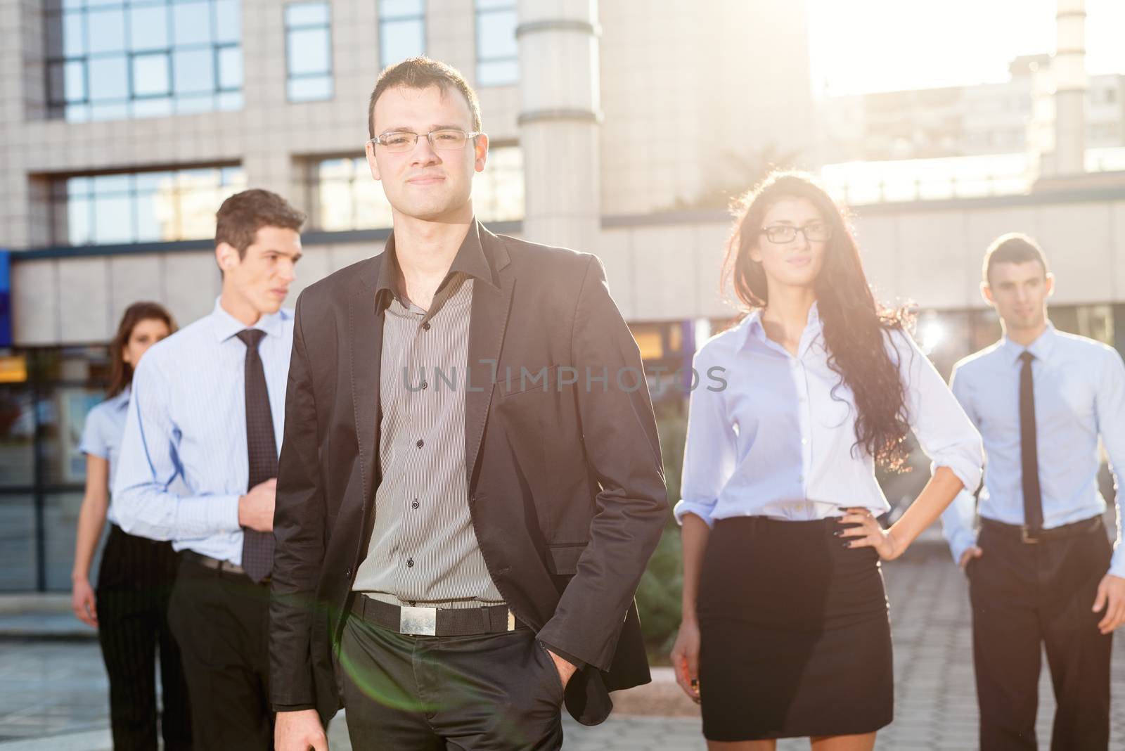 Young business team, elegantly dressed standing outside in front of office building. Looking at camera.