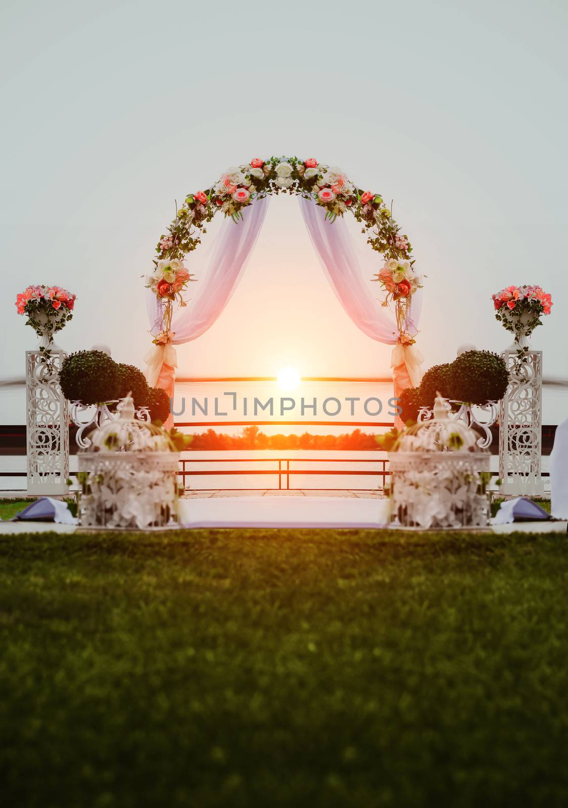 Wedding ceremony by the river at sunset. Arch decorated with flowers in the center of the composition