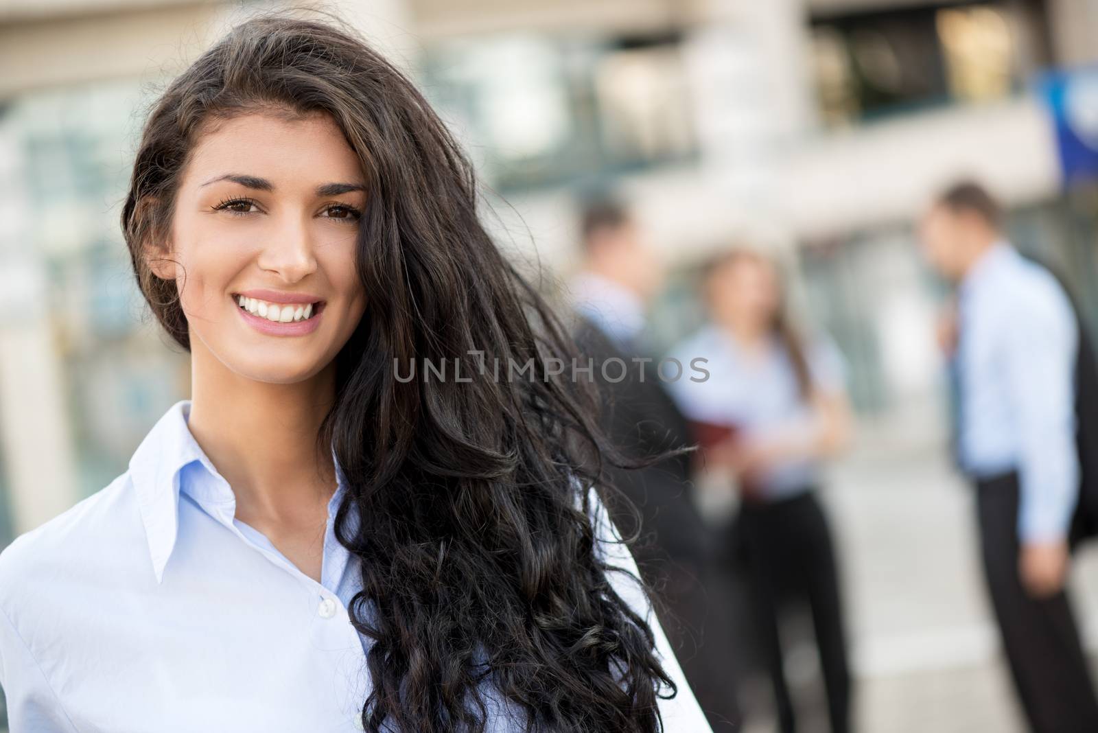 Close-up of portrait a young businesswoman standing in front of office building separated from the rest of the business team. Looking at the camera. 