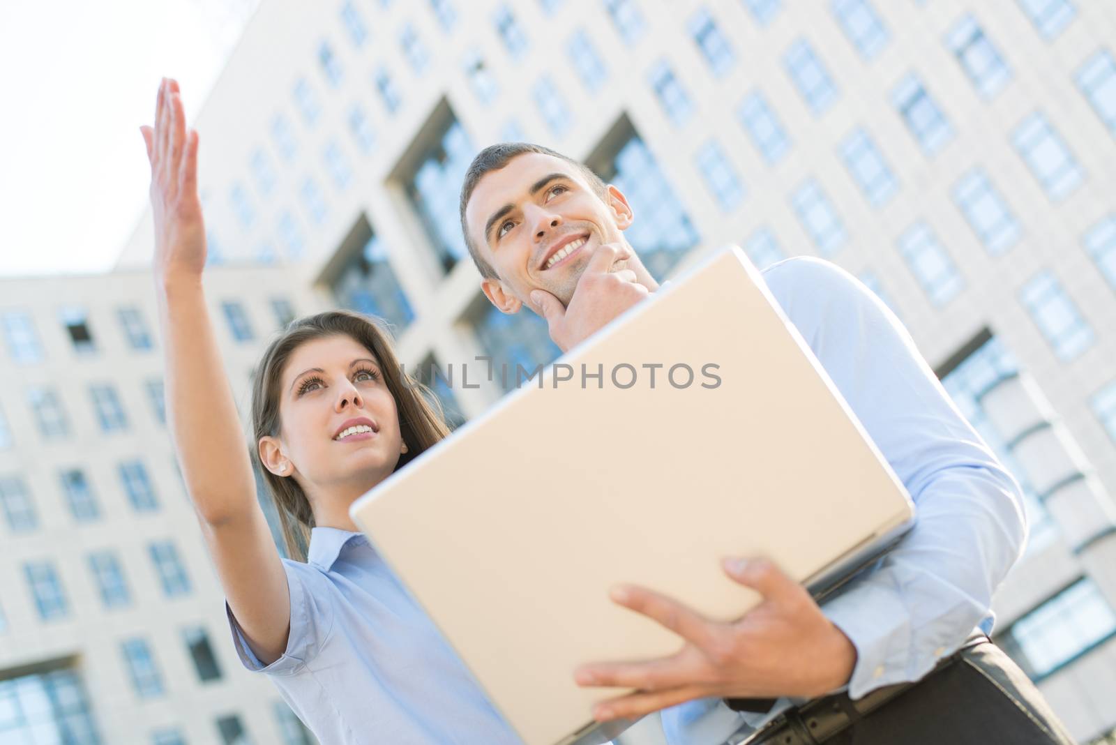 Young business couple with laptop, standing in front their company, look ahead at the height and thinking.
