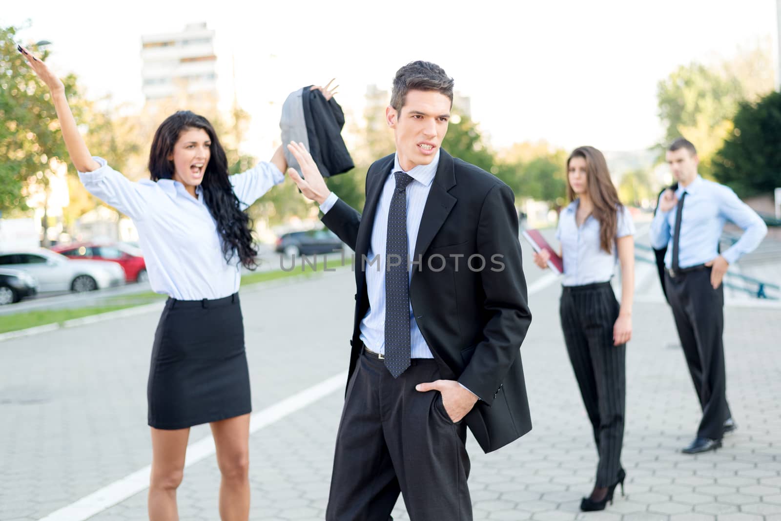 Young handsome businessman dressed elegantly indifferent waved his hand toward a young attractive businesswoman who yelling at him on the street in front of colleagues who viewed their fight.