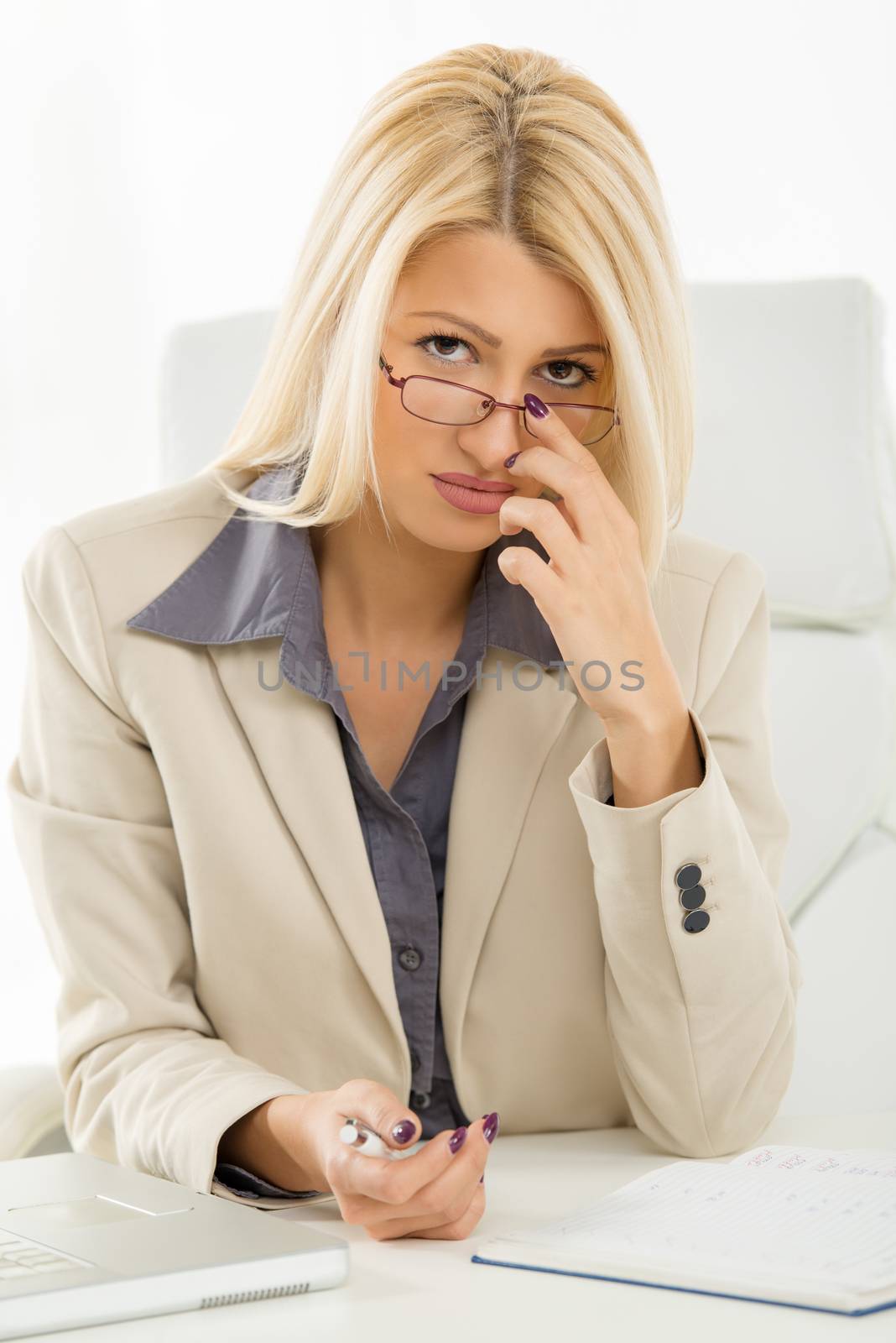 Young beautiful businesswoman with the glasses sitting at an office desk and looking at the camera adjusting glasses.