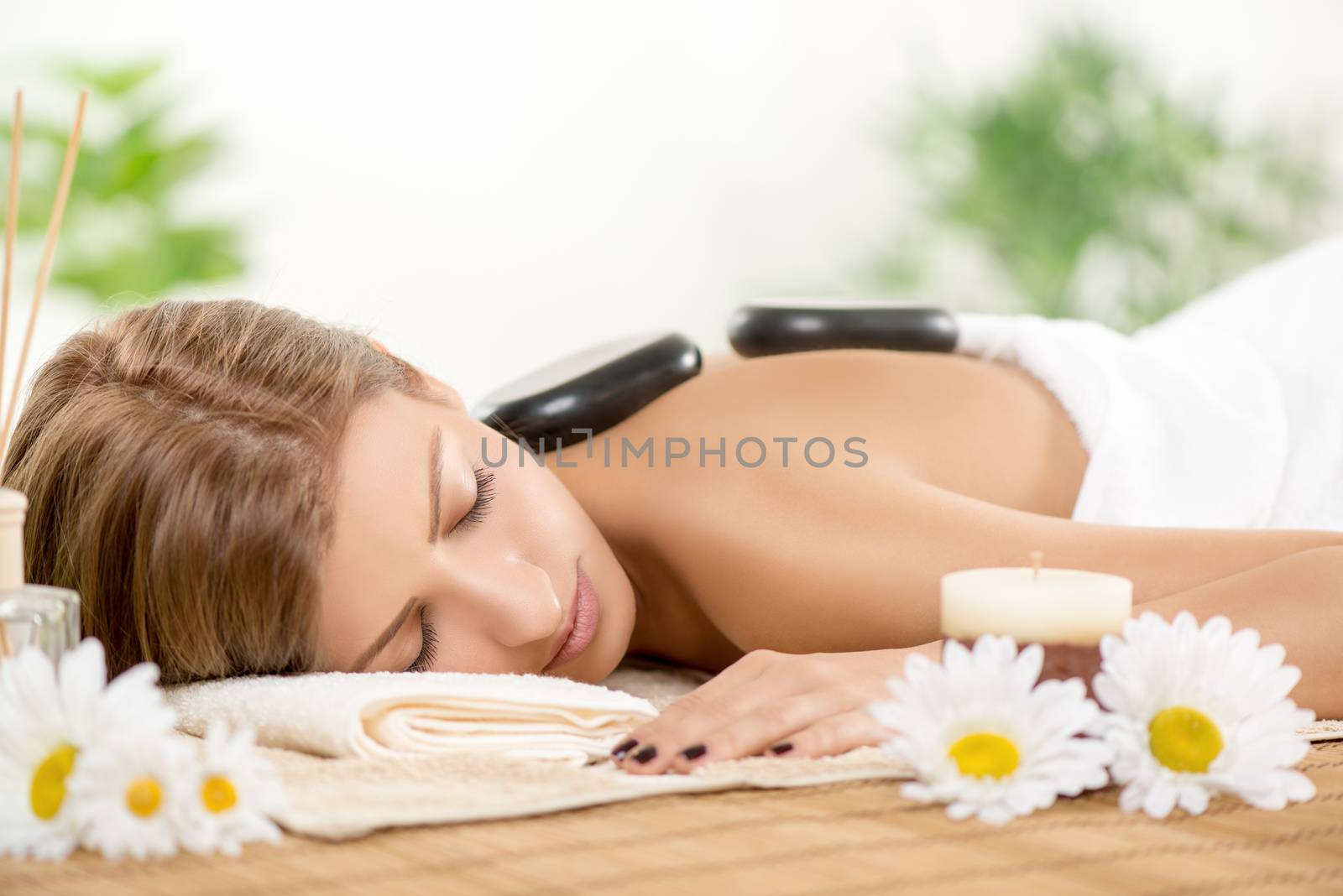 Young beautiful woman relaxing at spa centre. She is enjoying at stone massage.