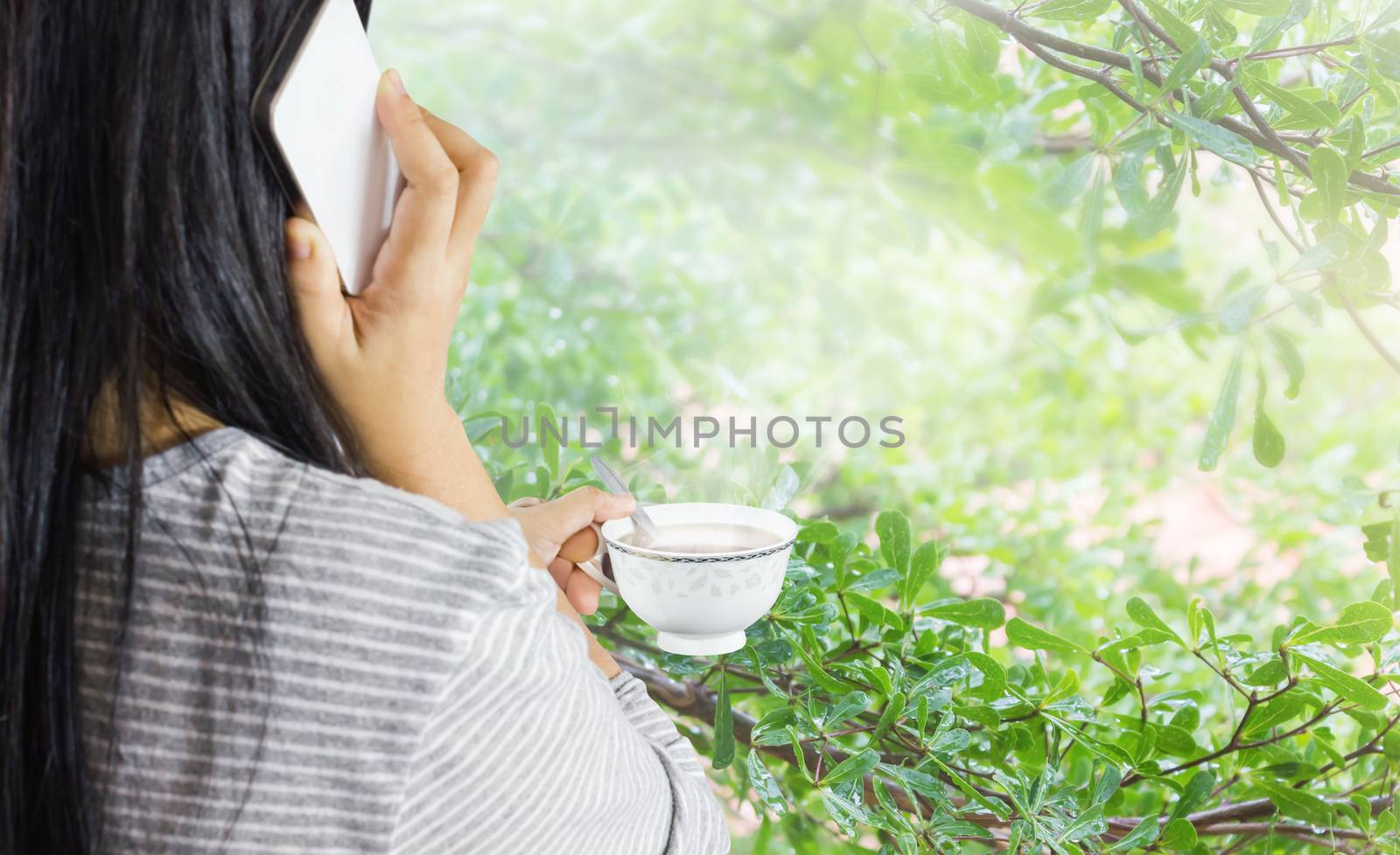 Focused at hot drink in hand of women, girl back or rare view with mobile phone, women hold cup of coffee and talking on mobile or smartphone in relax morning 