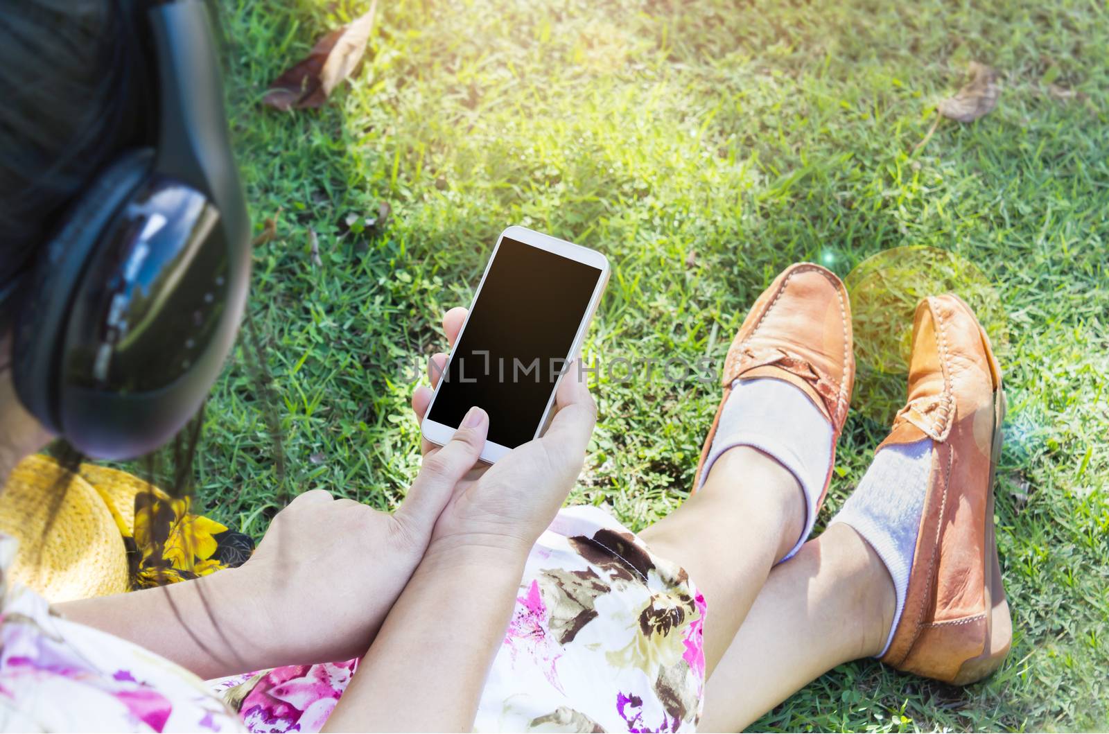 Women or girl with smartphone or cellphone in hand and finger press at blank screen, women sitting on grass field listen to music via headphone or watching media on internet with smartphone, girl play game on mobile in relax sunny day