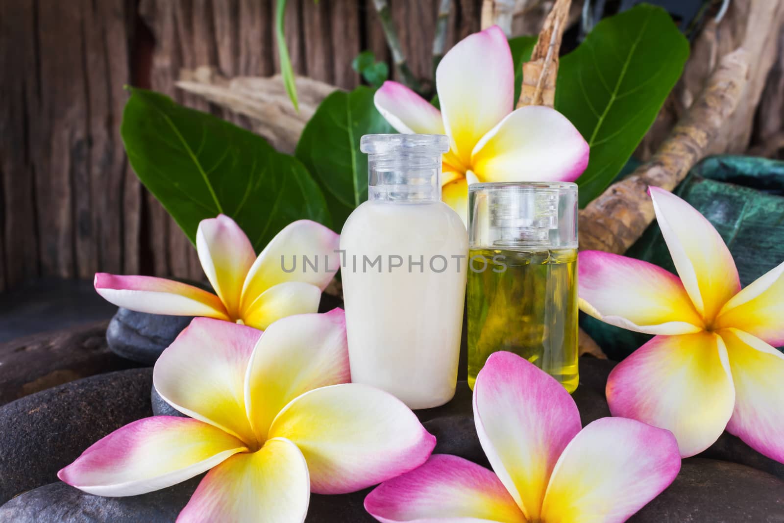 Mini set of bubble bath and shower gel liquid with pink white and yellow flowers plumeria or frangiani on pebble rock with green leaf and timber or wooden background, shampoo conditioner shower or body gel in relax spa mood
