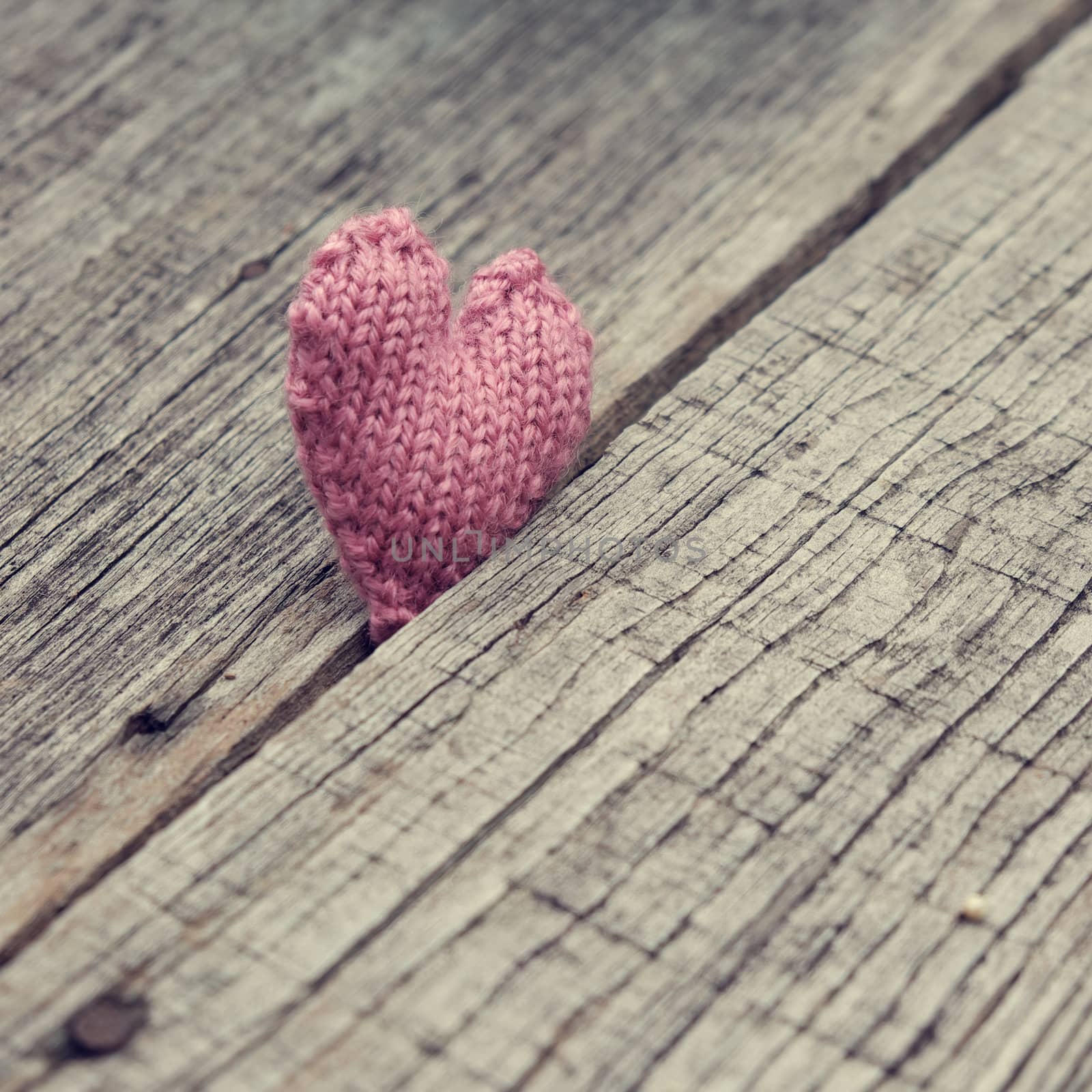 Lonely heart on wooden background, symbol of love with pink knitted heart in vintage color