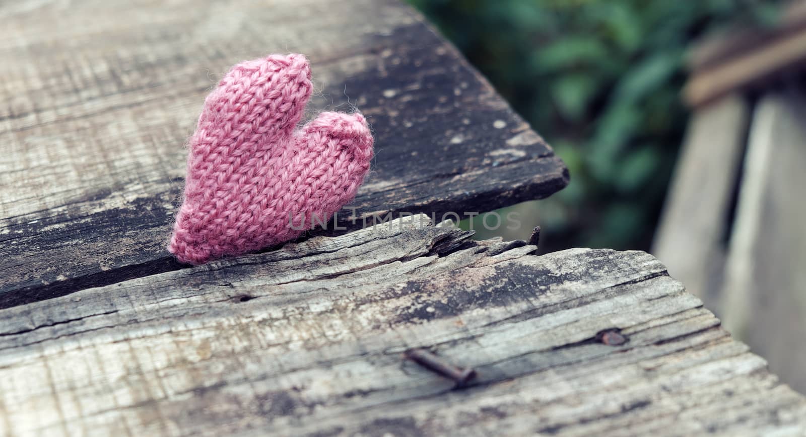 Lonely heart on wooden background, symbol of love with pink knitted heart in vintage color