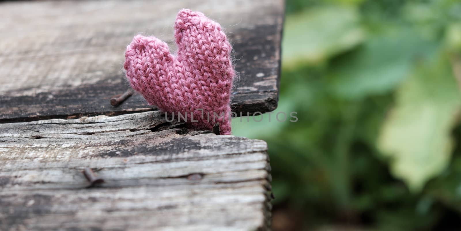 Lonely heart on wooden background, symbol of love with pink knitted heart in vintage color