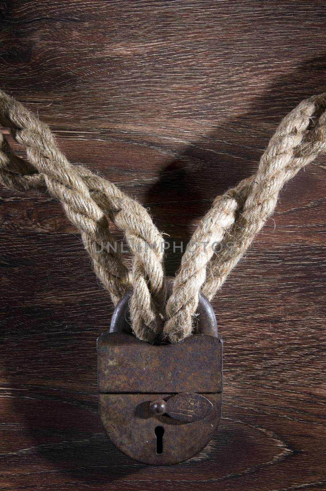 Old rusty lock with rope on wood background.