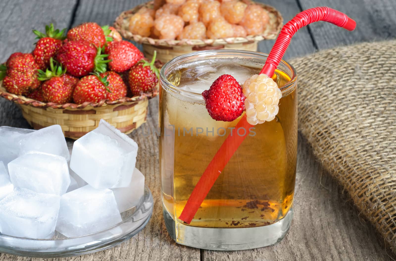 Iced tea with yellow raspberries, strawberries and ice cubes on the old boards.