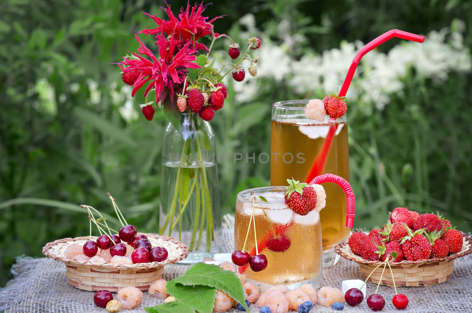 Iced tea and different berries on the table in the garden.