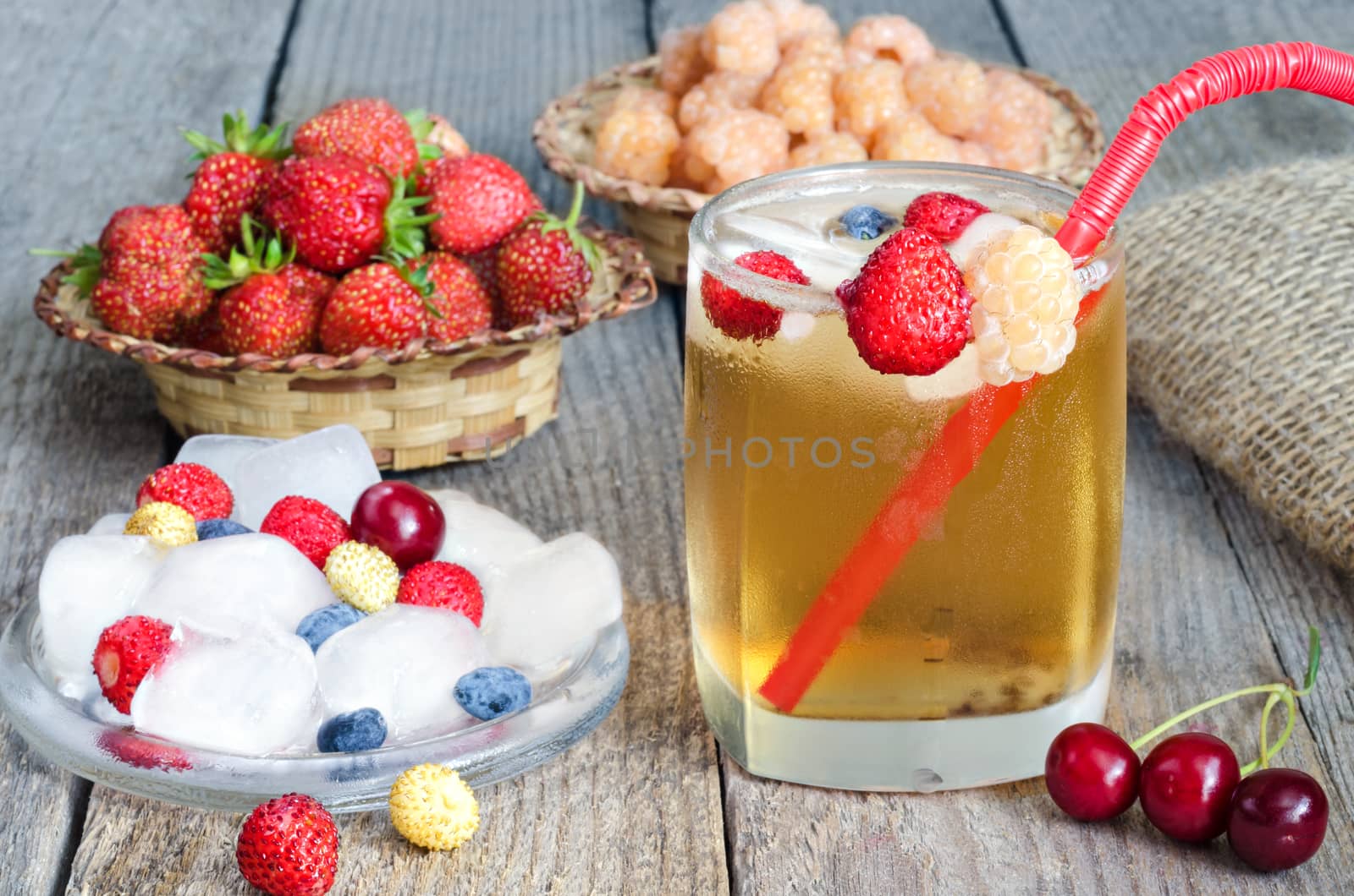 Iced tea with different berries and ice cubes on the old boards.