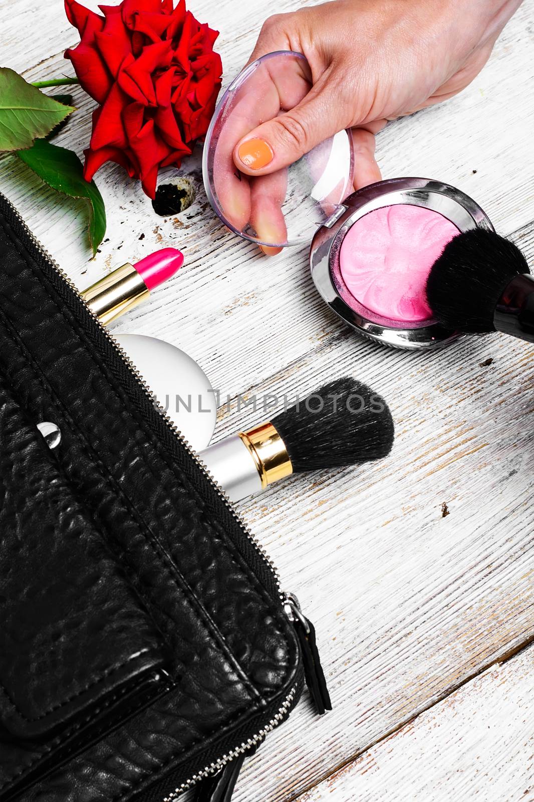 Women bag with lipstick,powder and cosmetics and a bright red rose