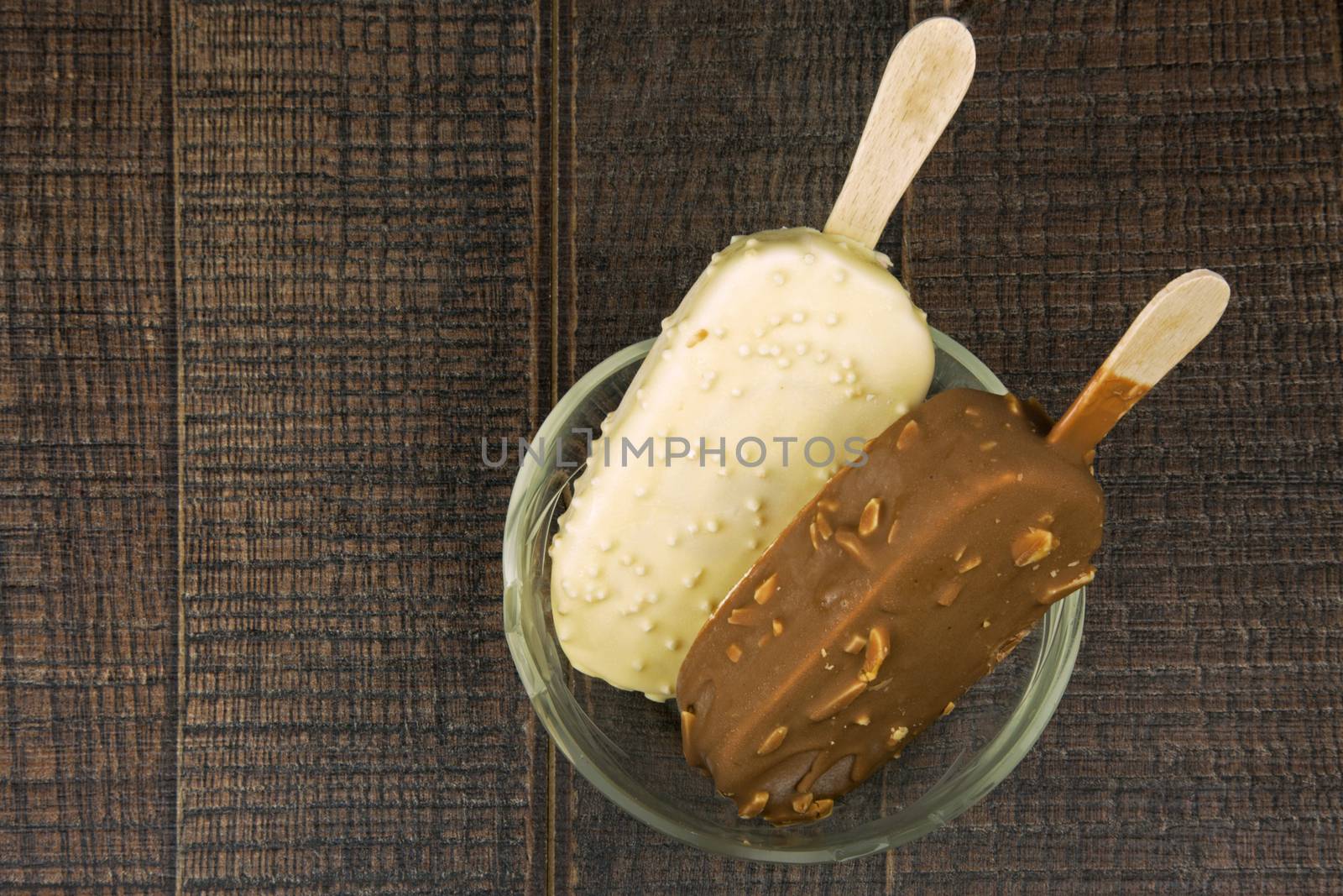 Two Ice cream ion a stick in a glass bowl on a wooden ,vintage table.Flat,horizontal view.