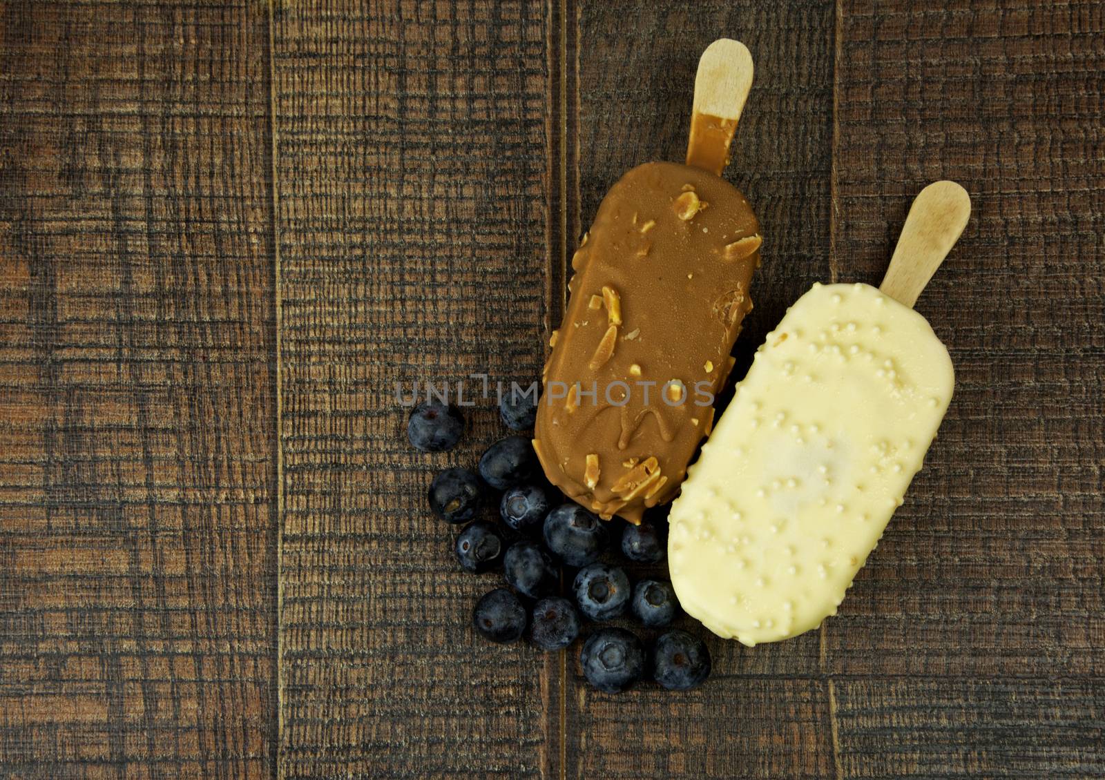 Two ice cream on a stick , vanilia and strawberry,with cranberries on a wooden table in vintage style.Flat, horizontal view.