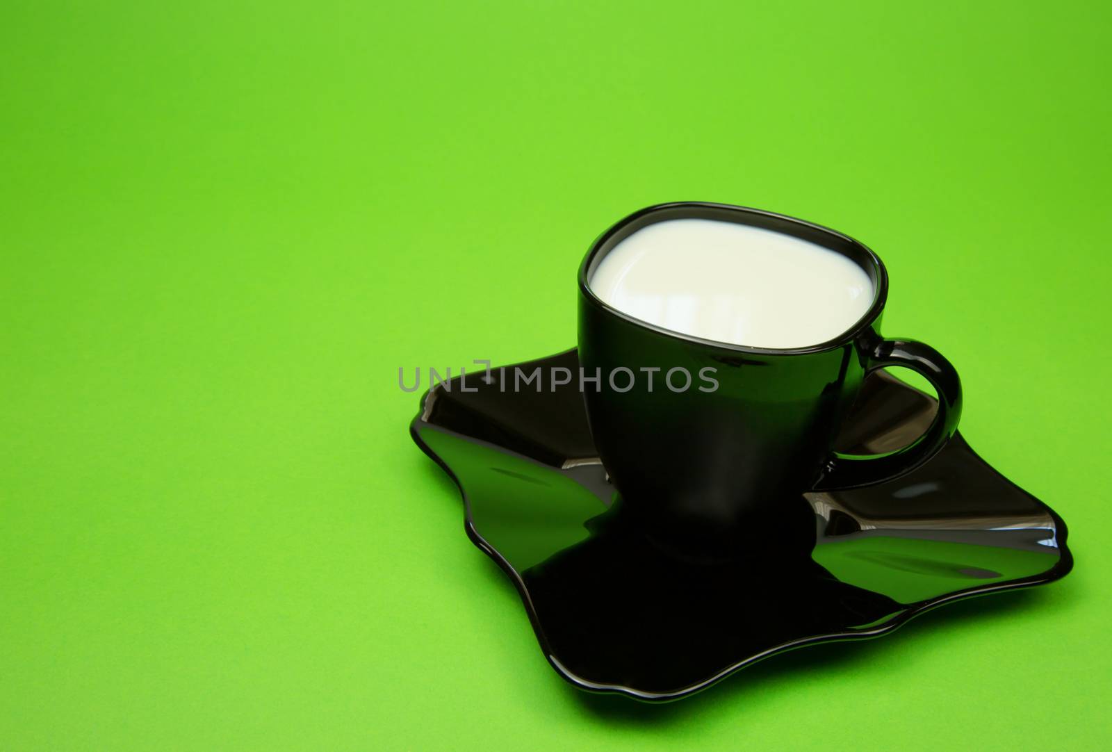 Black cup of milk on a black saucer isolated on a bright green background. Horizontal