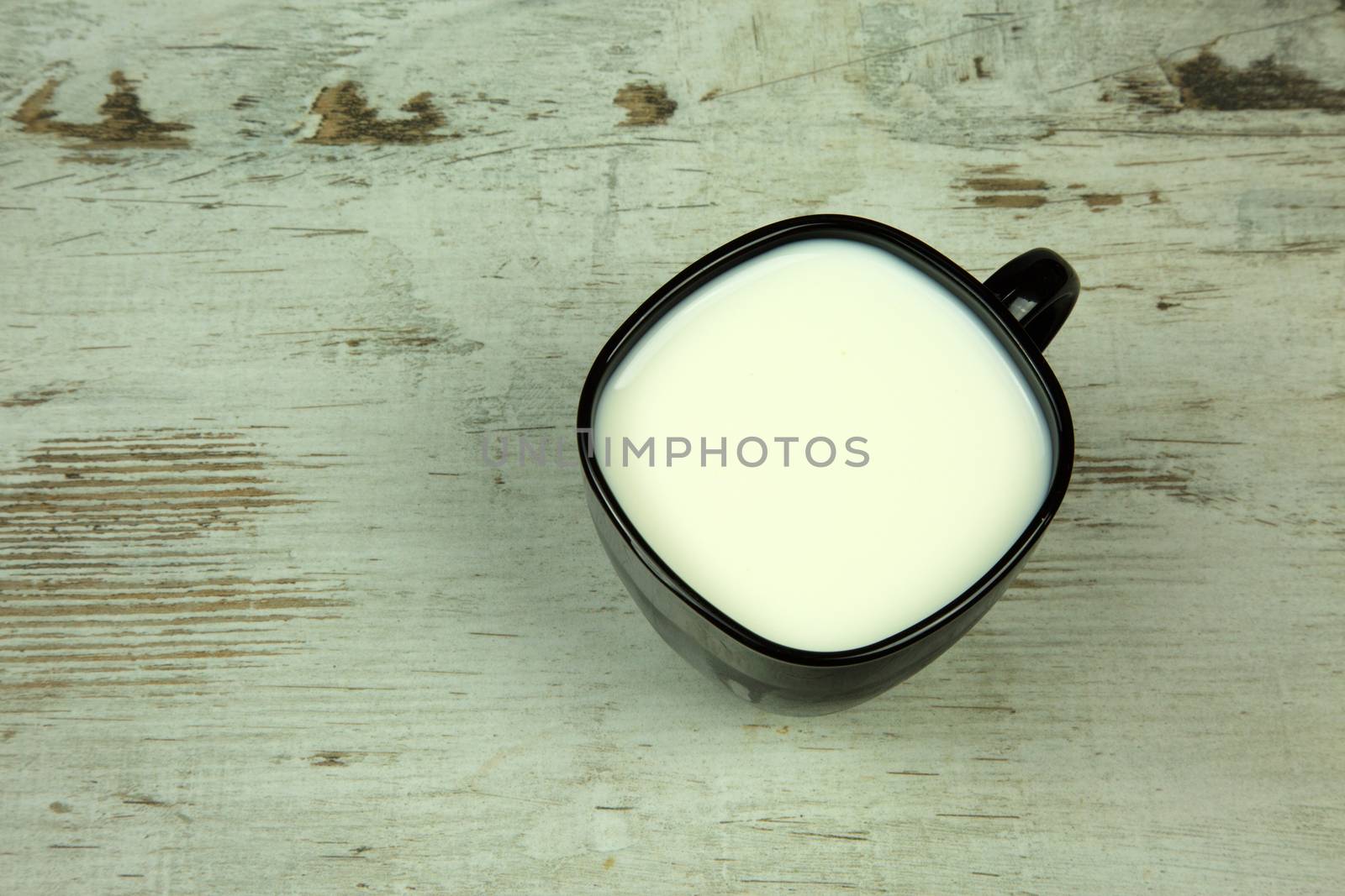 Black full cup of milk on a light, old wooden table in vintage style. Flat, horizontal view.