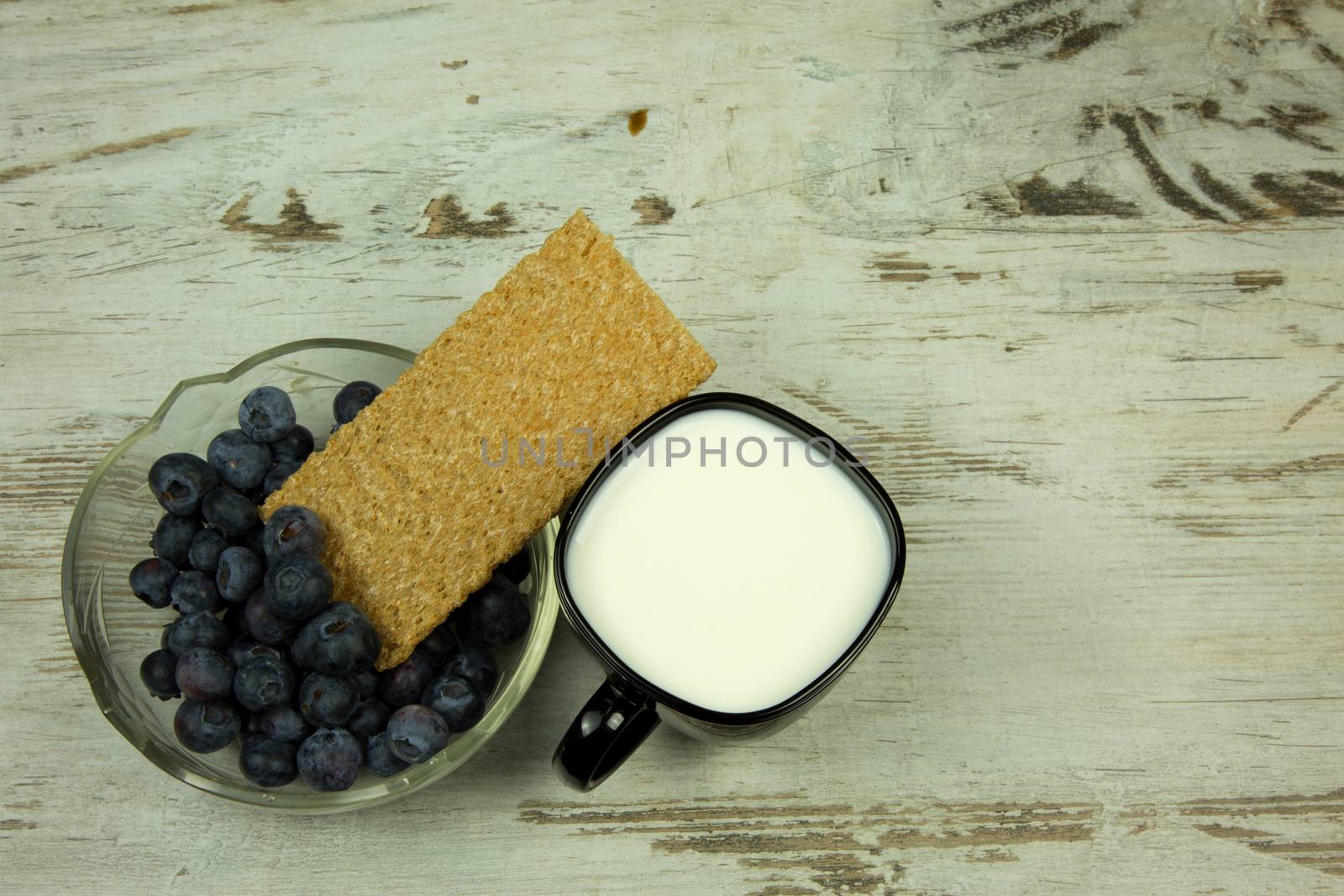 Cup of milk and crisp bread with cranberries in glass bowl on light,wooden table in vintage style.Flat,horizontal view.