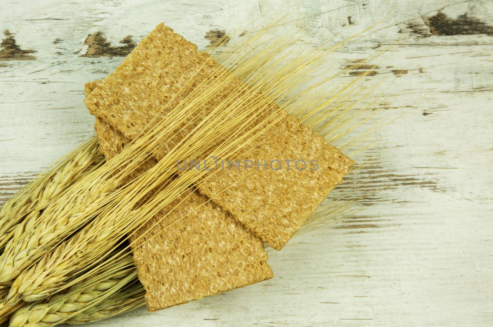 Two crisp bread and ears of corn on wooden background i  vintage style. Flat,horizontal view.