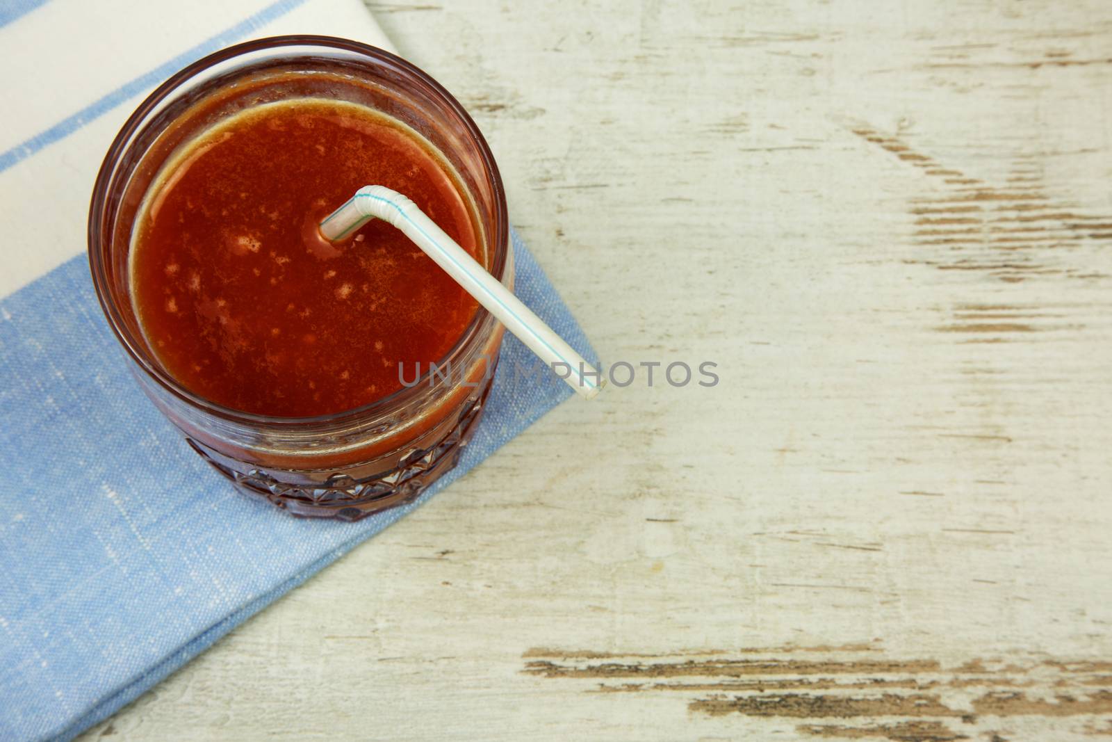 A glass of fresh tomato juice with a straw, standing on a napkin and an old wooden table in vintage style. Flat, horizontal view.