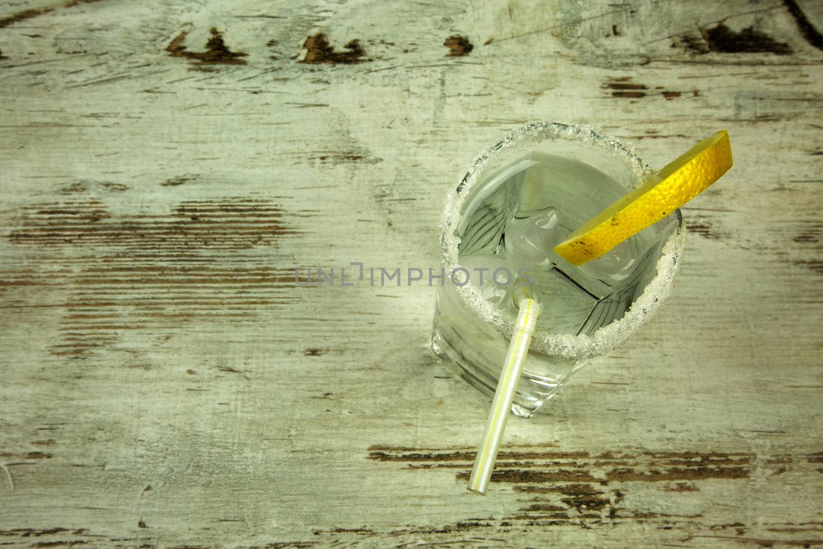 Glass from the shores of decorative sugar, full of cold water with ice and lemon, refreshing drink for the summer on an old wooden table in vintage style with space for text. Flat, horizontal view.