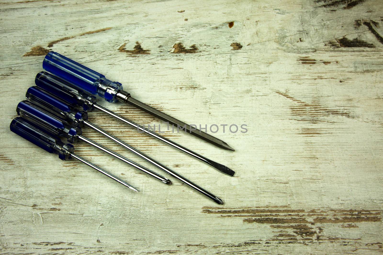 A set of five different screwdrivers on an old wooden table in vintage style. Flat, horizontal view. Possible to insert the text.