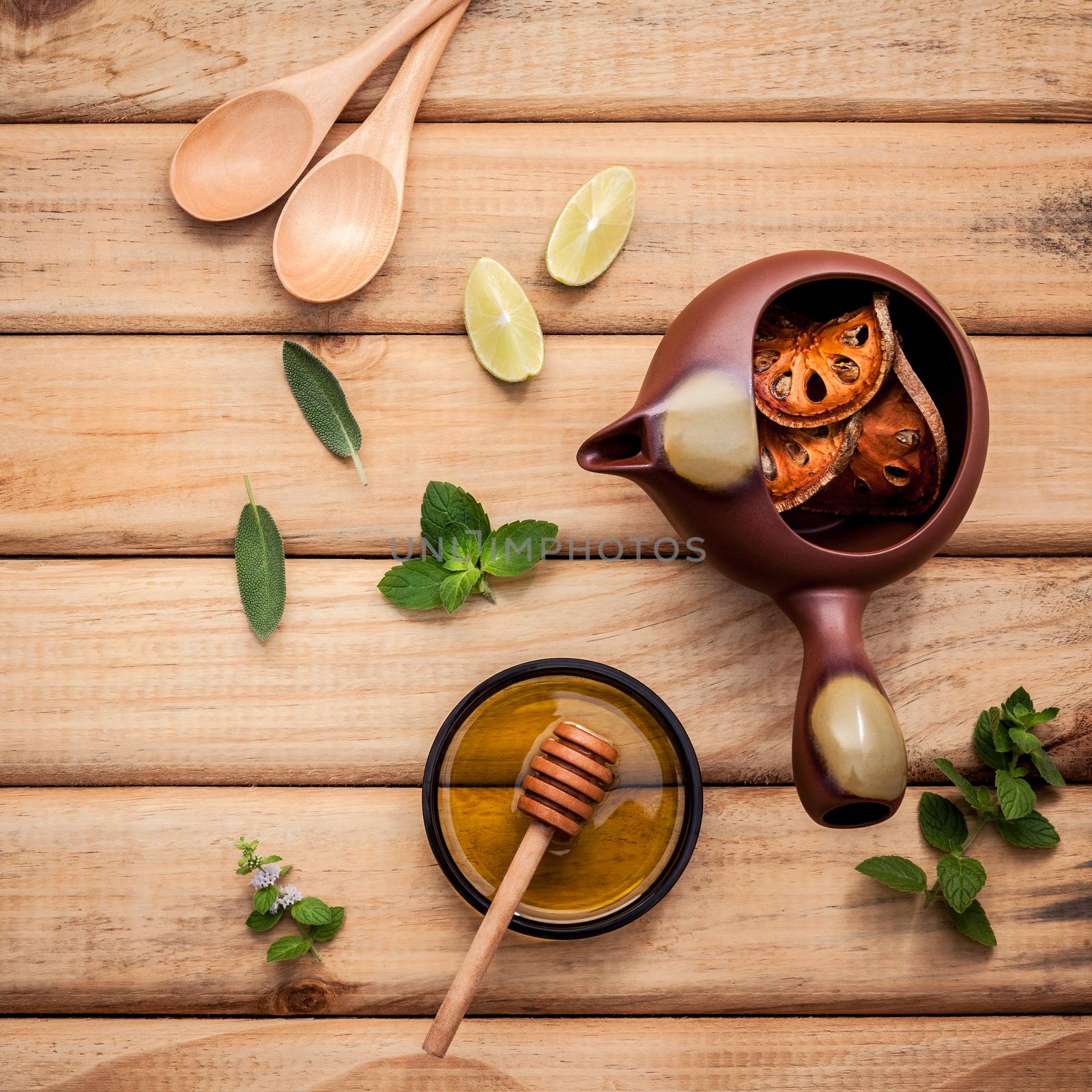 Herbal tea pot with fresh herbs sage ,peppermint ,dried indian bael, honey and lime slice on rustic wooden background.