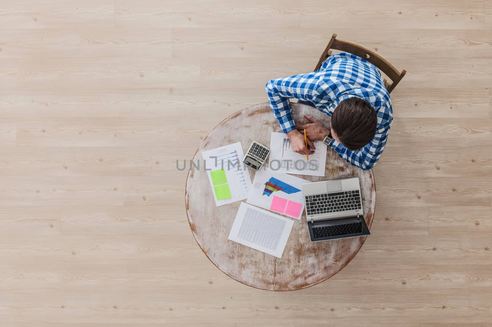 Man working on a wooden table with laptop and financial documents, top view