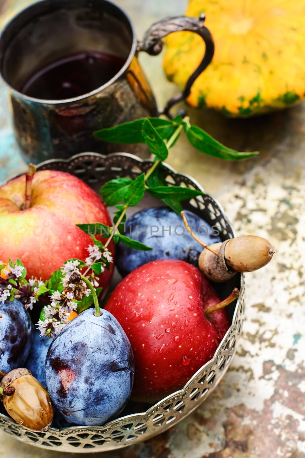 Stylish metal bowl with apples,plums and acorns in the autumn still life