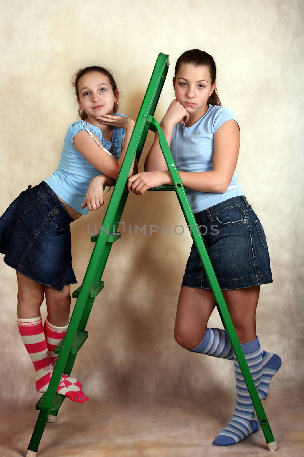 Portrait of the young girls with step-ladder on a yellow background