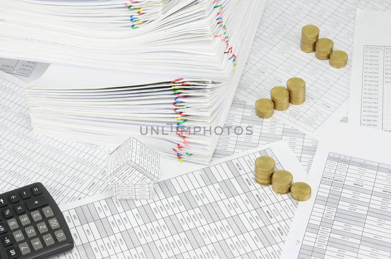 House and step pile of gold coins on finance account have calculator and pile overload paperwork of report with colorful paperclip as background.