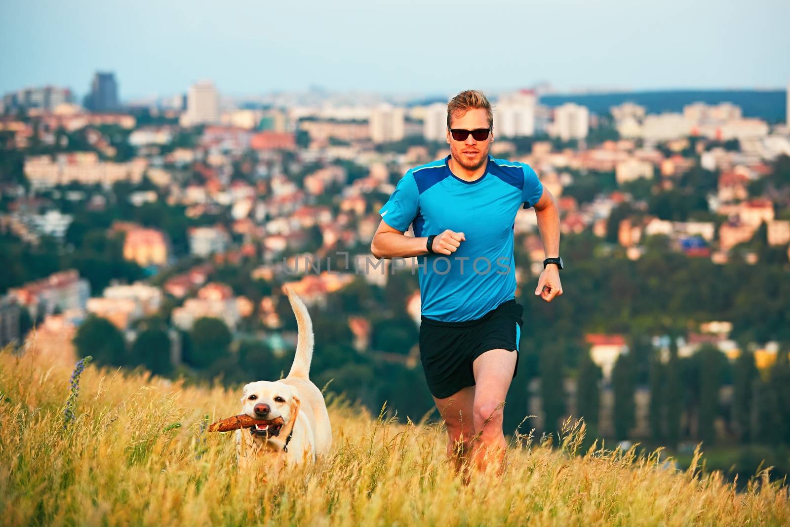 Sport lifestyle with dog. Athletic young man and labrador retriever are running on the hillside outside the city. Prague, Czech Republic.