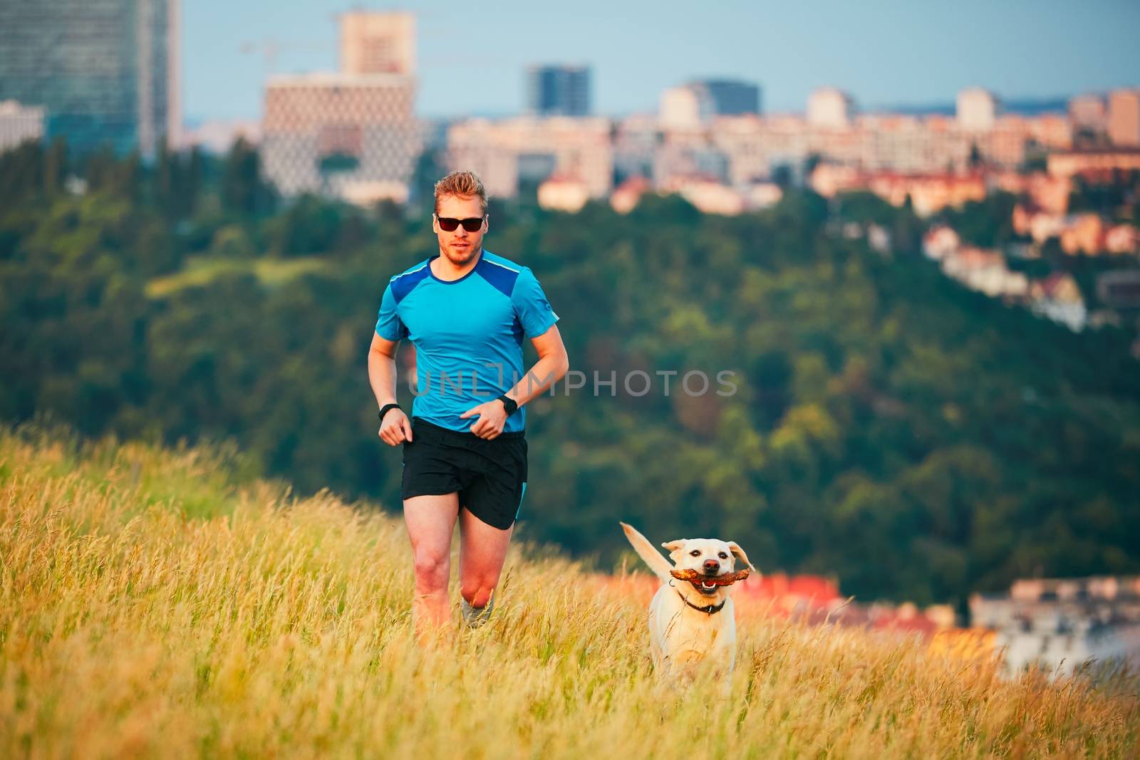 Sport lifestyle with dog. Athletic young man and labrador retriever are running on the hillside outside the city. Prague, Czech Republic.