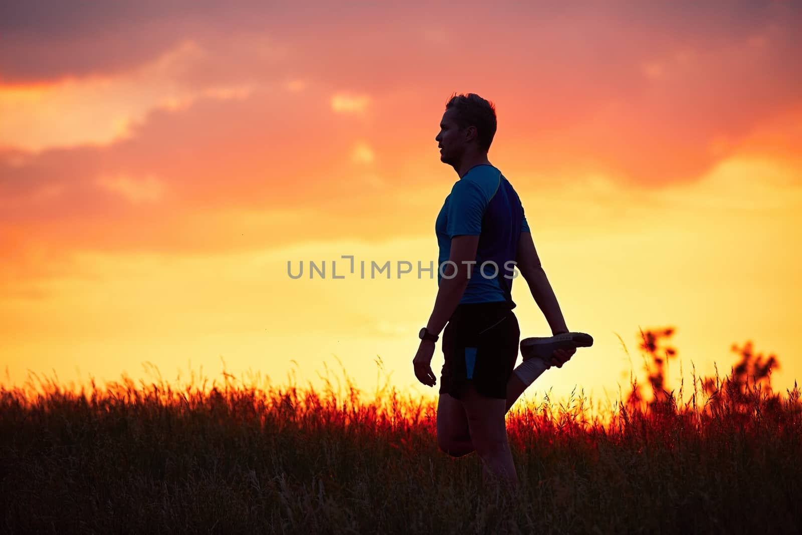 Silhouette of runner. Outdoor cross-country running. Male runner is doing stretching exercise and preparing for workout during golden sunset.