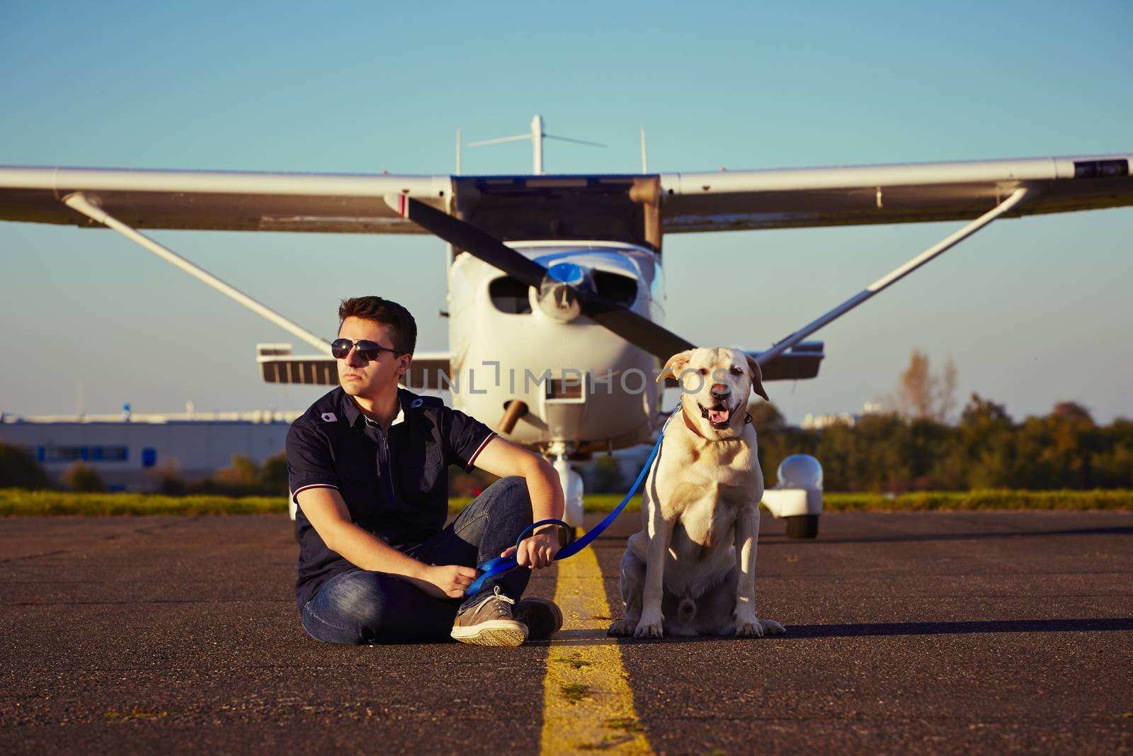 Young pilot with dog are sitting in front of the airplane