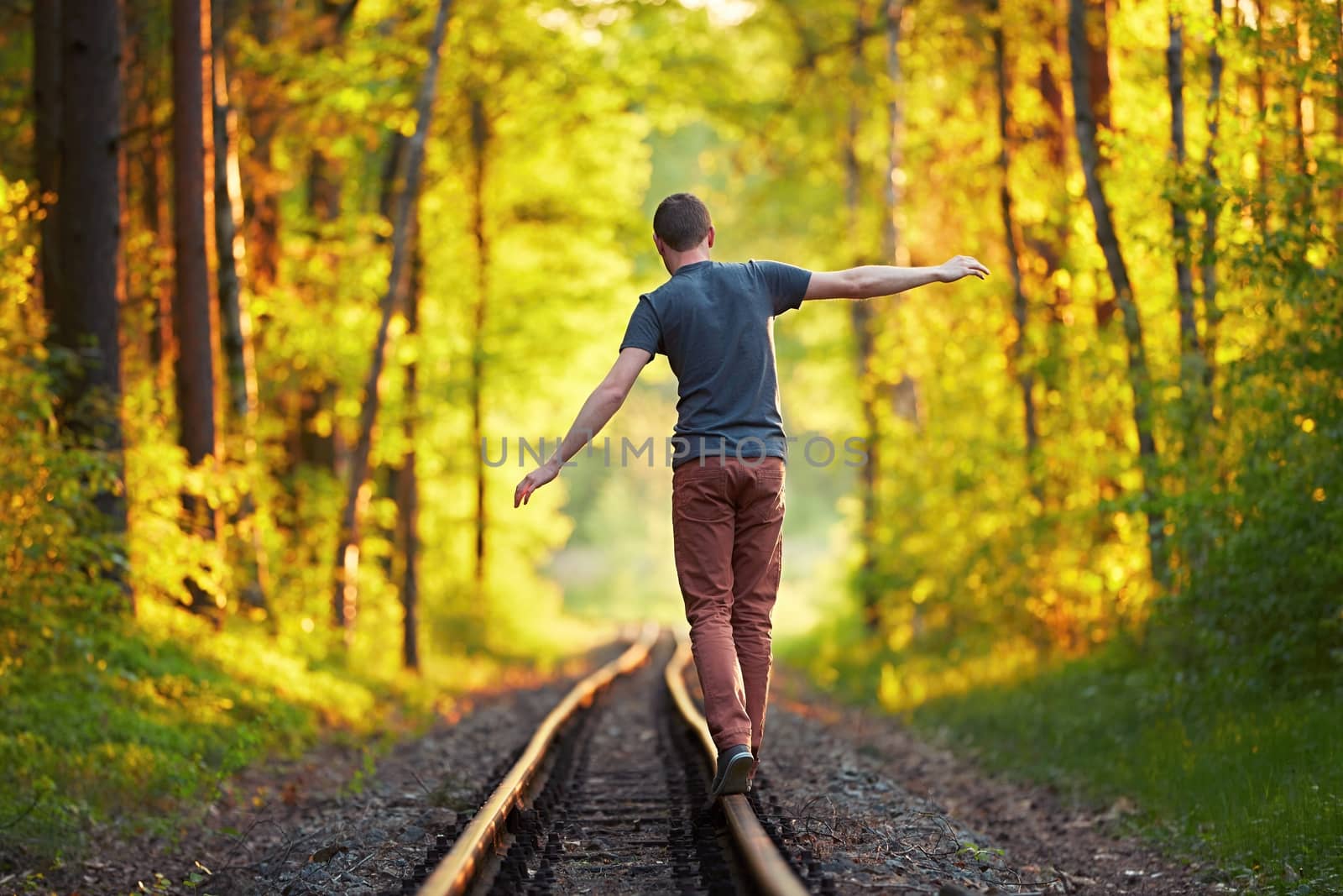 Summer time - Young man enjoying on the trip. Walk on the railroad track in forest at the sunset. 