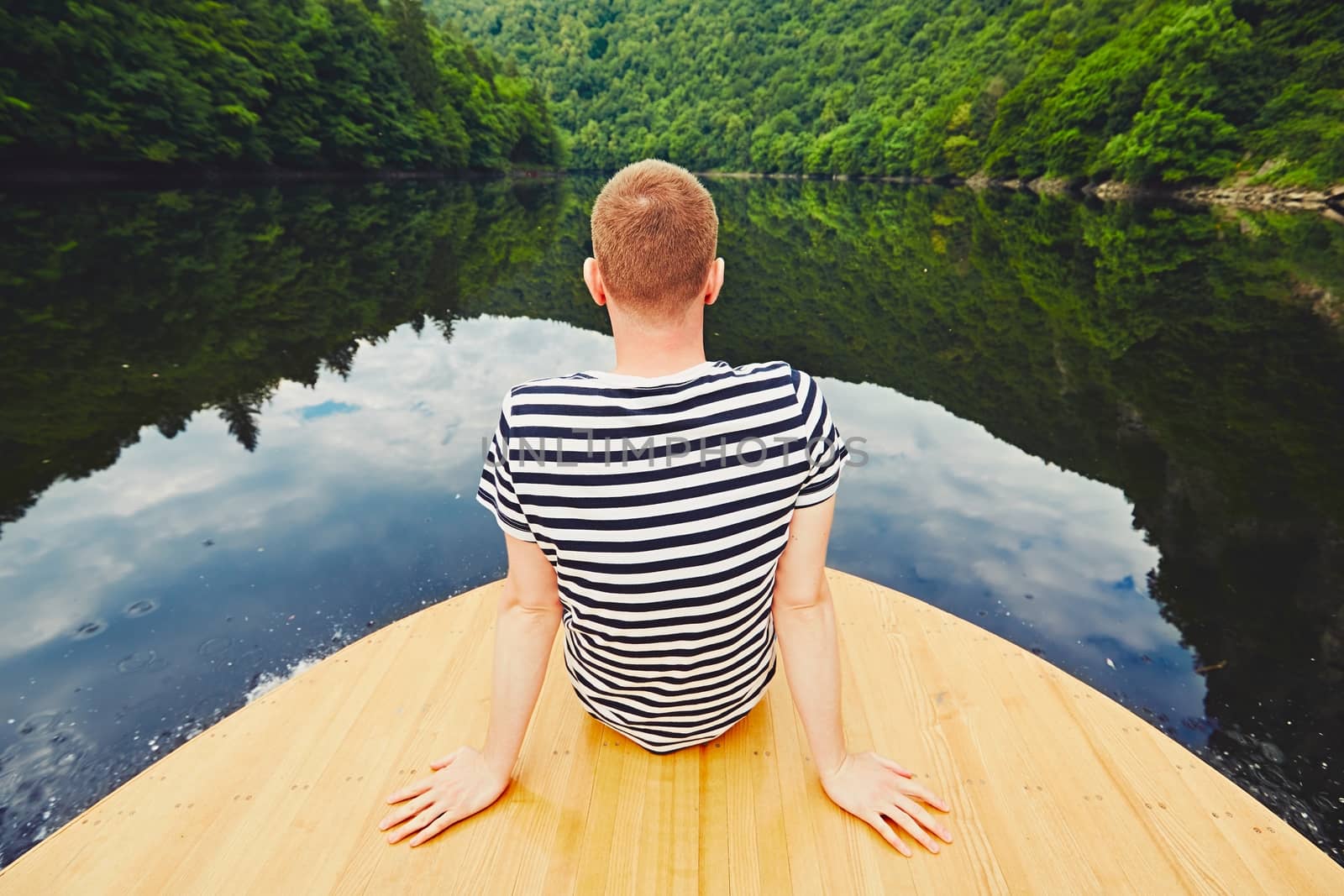 Vacation trip on the river. Handsome man is sitting on the prow of the boat. 